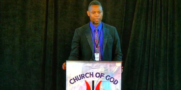 Man speaking at a Church of God podium with a microphone.