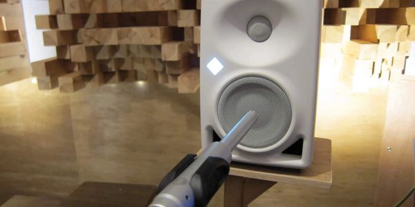 A white speaker with a microphone in front in a wooden acoustic room.