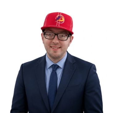 Man in a suit and red cap smiling.