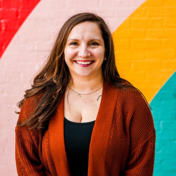 Ashley Scheetz standing in front of a vibrantly colored wall smiling.
