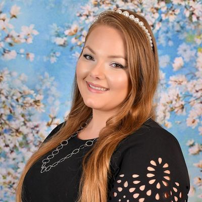Haley Gunther LMHC smiling in a black dress with a pearl headband with a flower backdrop