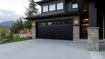 Modern house with a dark garage door and stone pillars.