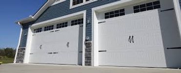 Two white garage doors with decorative black hardware on a blue house.