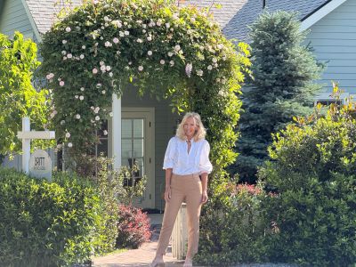 A woman stands in front of a flower-covered archway.
