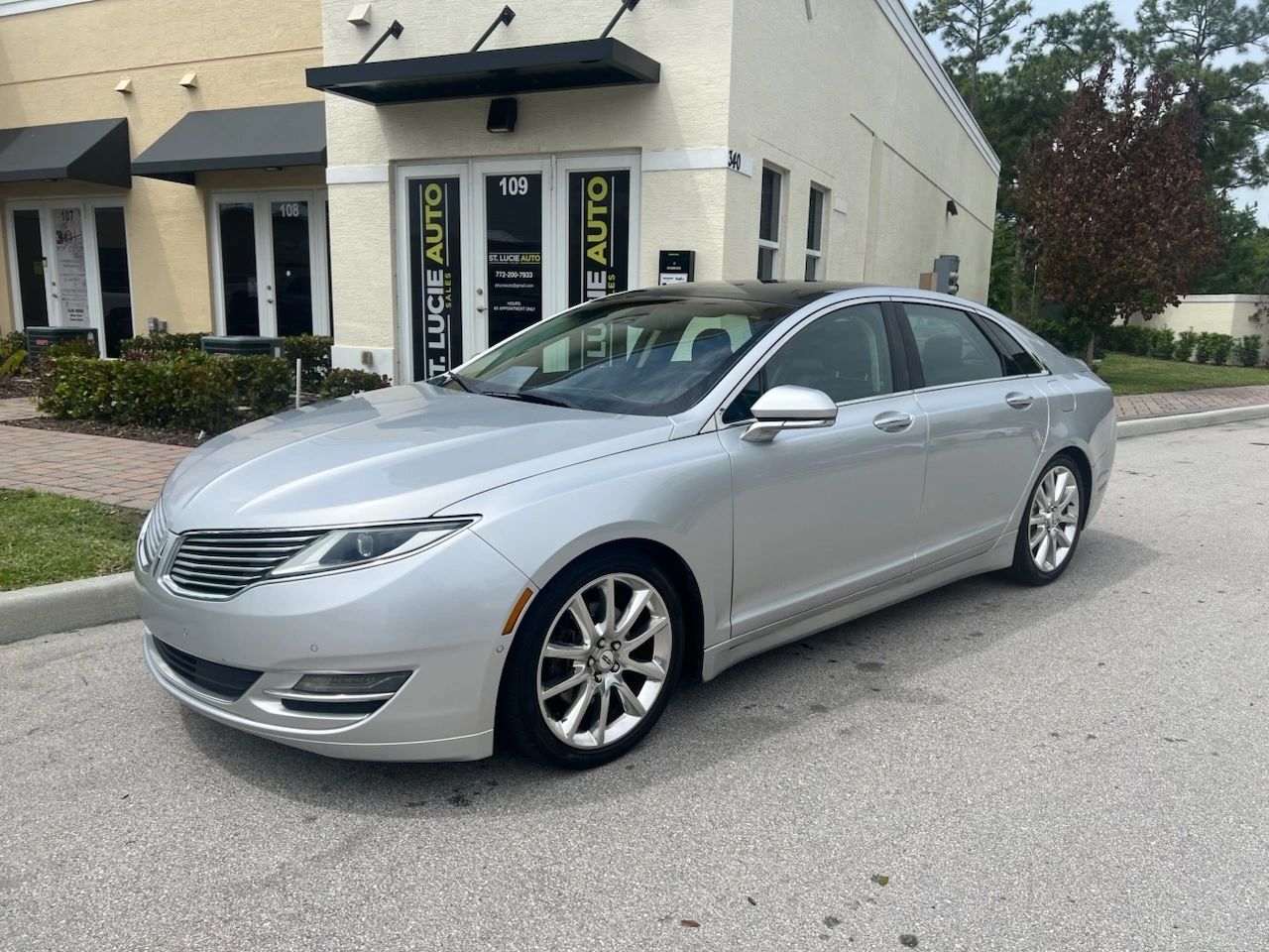 Silver luxury sedan parked outside an auto sales shop.
