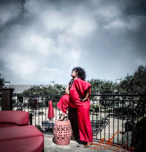 Woman in vibrant red outfit posing confidently on a balcony under cloudy skies.