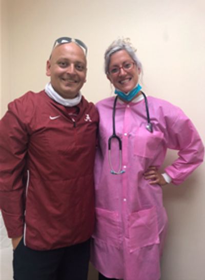 Two smiling individuals posing together, one in a pink medical coat with a stethoscope.