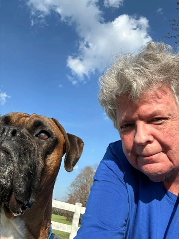 Man in blue shirt with brown dog outdoors.