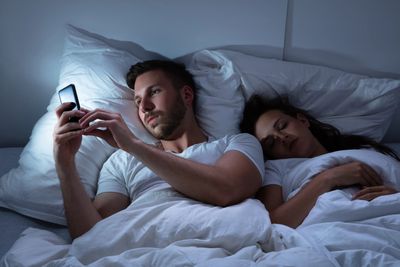 Man using his cellphone while his partner is asleep