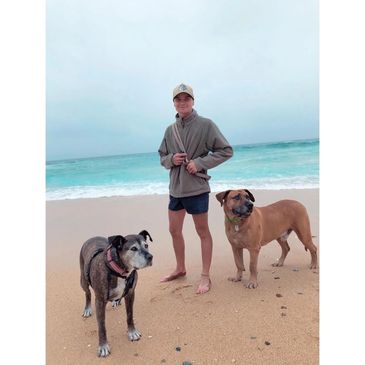 A man standing barefoot on a beach with two dogs.
