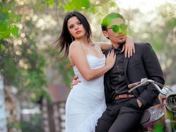 Couple posing stylishly outdoors with the man on a motorcycle.
