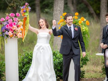 Bride and groom joyfully celebrating their wedding outdoors with vibrant floral decorations.