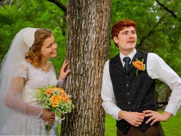 Bride and groom posing playfully by a tree in a garden.