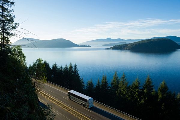 Bus driving on a coastal highway with mountains and water.