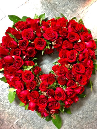 Heart-shaped wreath of red roses with green leaves.
