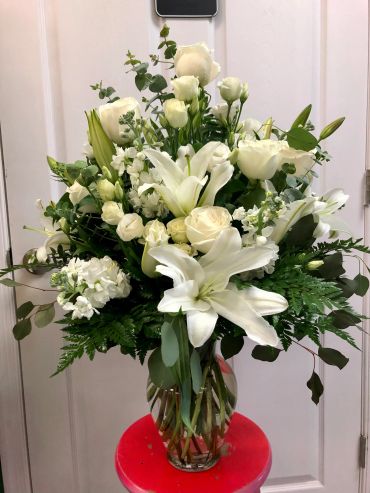Elegant bouquet of white flowers in a clear vase on a red stool.