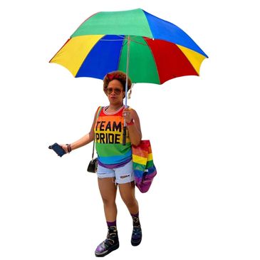 Person holding a rainbow umbrella wearing a Team Pride shirt.