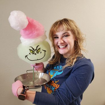 Woman smiling holding Grinch-themed cotton candy with pink gloves.