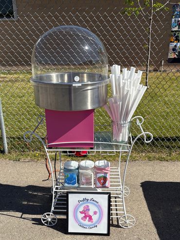 Cotton candy machine setup with flavors and sticks on a sunny day.