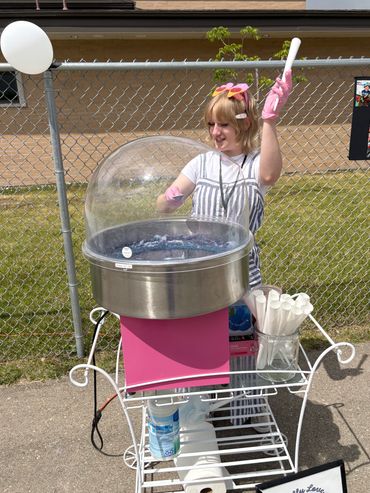 Person making cotton candy at an outdoor event with pink gloves and decorations.