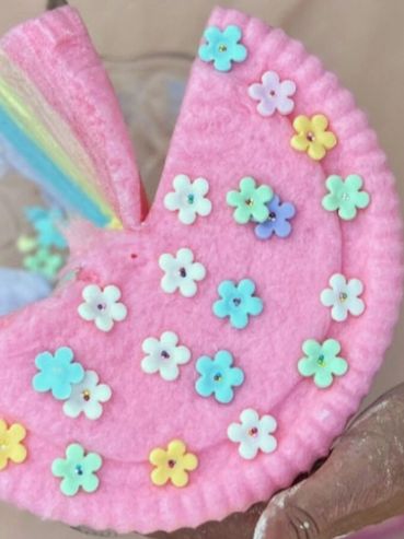 A pink felt craft decorated with colorful flower appliques, held in hand.