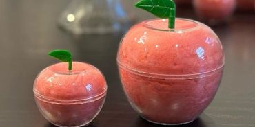 Two apple-shaped containers filled with pink cotton candy on a table.