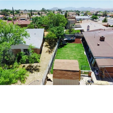 Aerial view of suburban backyards with trees and green lawns under a clear sky.