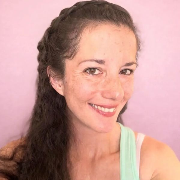 Smiling woman with long dark hair against a soft pink background.