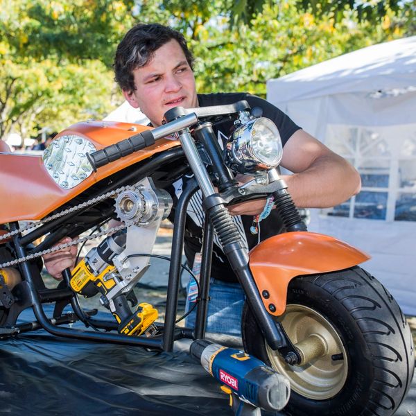 Man working on an orange motorcycle with tools outdoors.