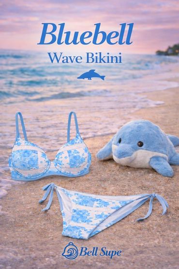 Bluebell Wave Bikini with floral pattern on a sandy beach beside a plush dolphin toy.