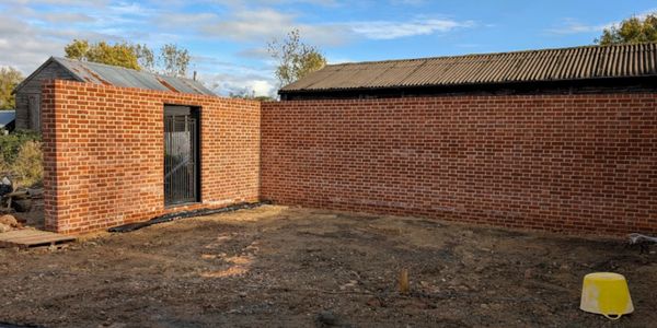 A brick wall enclosing an empty dirt area with a yellow bucket.