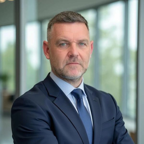 Confident businessman in a navy suit posing indoors with arms crossed.