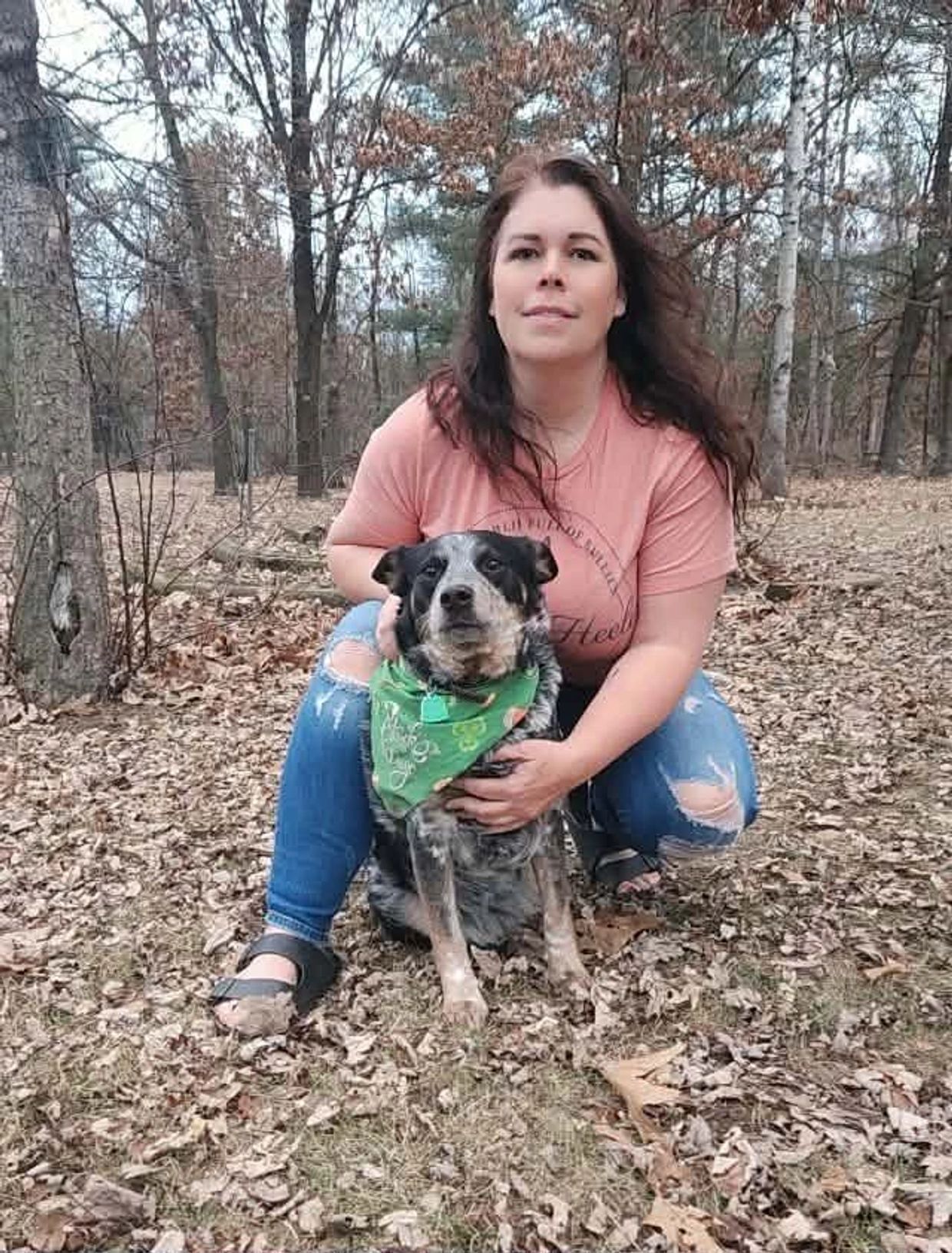 Woman sits with her dog in the woods.