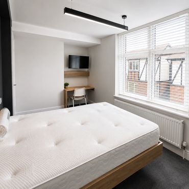 Minimalist bedroom with a large mattress and a small desk beneath a wall-mounted TV.
