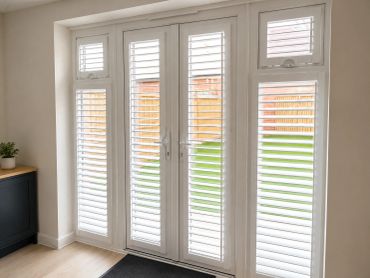 White plantation shutters on glass doors and windows in a bright room.