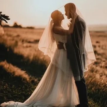 married couple standing in a field wearing wedding gown and tuxedo holding each other at sundown 