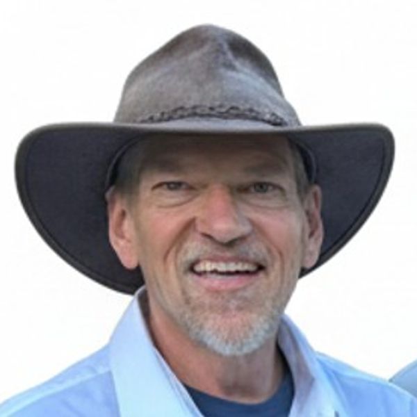 Smiling man wearing a wide-brimmed hat and blue shirt.