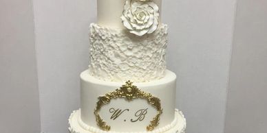 4-tier white wedding cake with textured fondant, white flowers, and gold accents