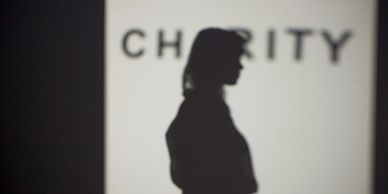 Silhouette of a person in front of a blurred 'CHARITY' sign.