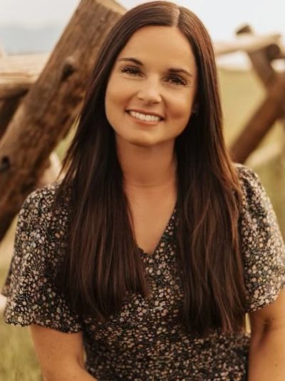 Smiling woman with long dark hair outdoors by wooden fence.