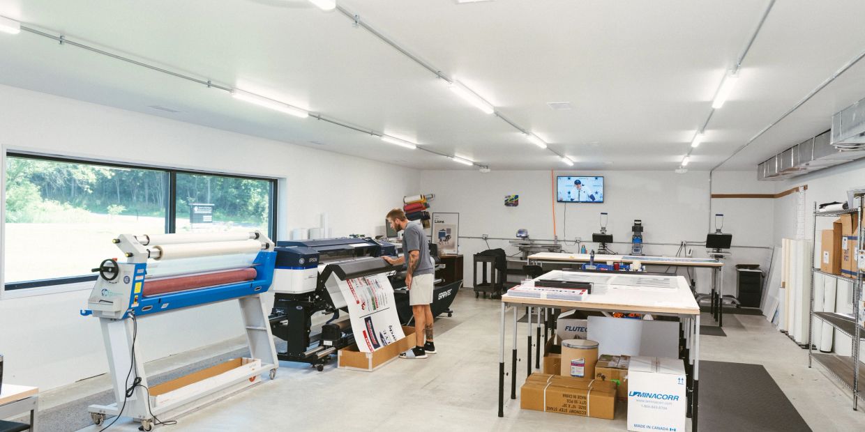 Complete Team Outfitter employee monitoring a large-format printer in the sign department.
