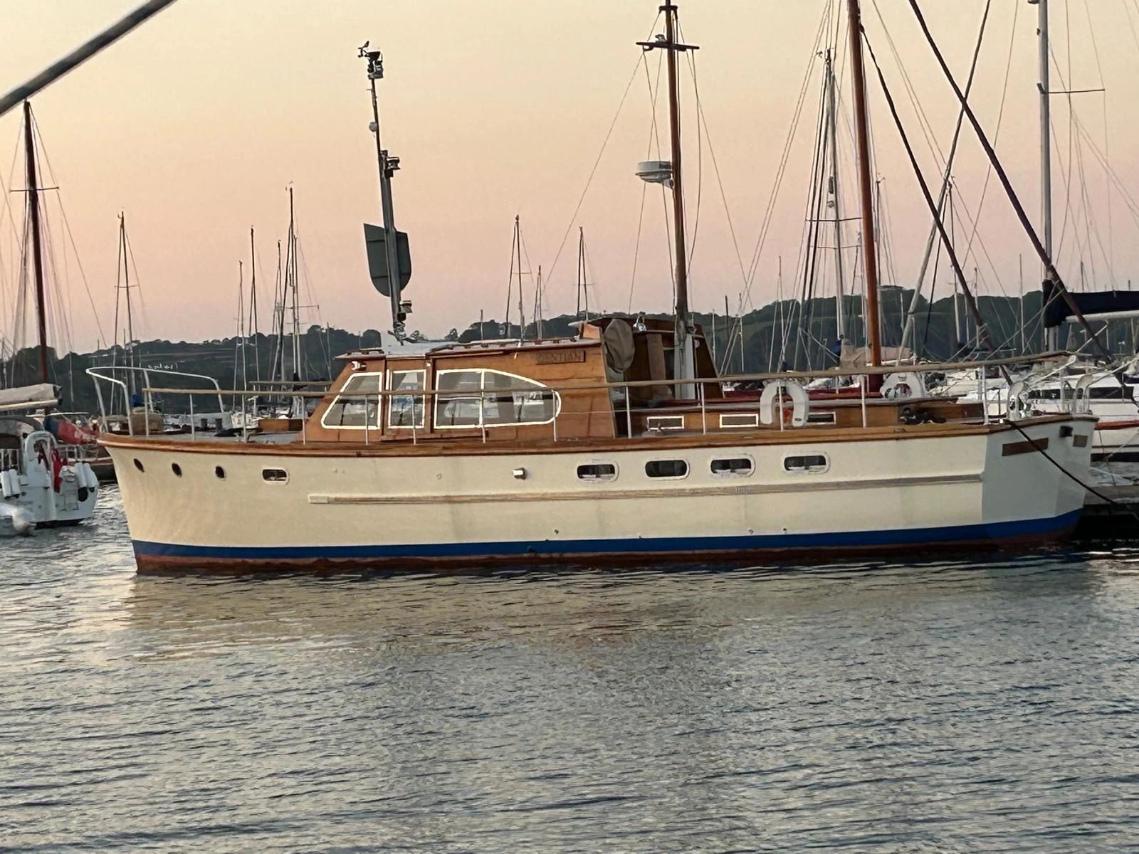 Classic wooden motor yacht docked at sunset in a marina.