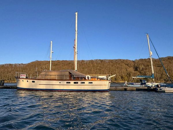 A classic wooden sailboat docked by a marina under clear blue skies.