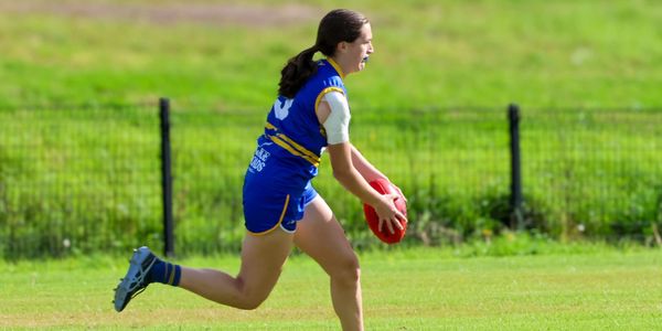 Female athlete in blue runs with a football on a grassy field.