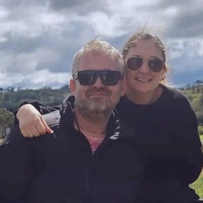 A smiling couple wearing sunglasses outdoors with a cloudy sky.