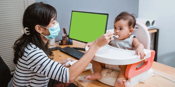 Woman wearing mask feeding baby in an office setting.