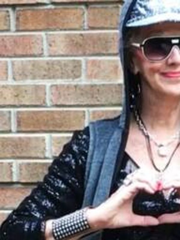 Person making a heart shape with hands, wearing sunglasses and a cap.