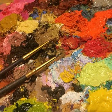 A close up photo of my very colourful artistic palette with oil paints and brushes.