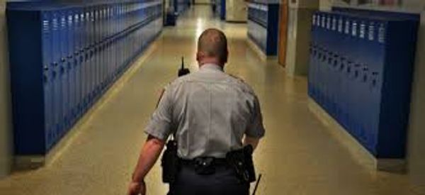 School security officer patrolling a hallway lined with blue lockers.