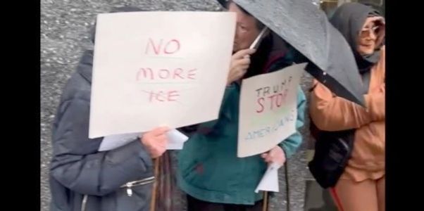 People holding protest signs under umbrellas on a rainy day.